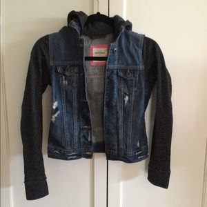 Jean jacket with gray sweatshirt sleeves and hood.
